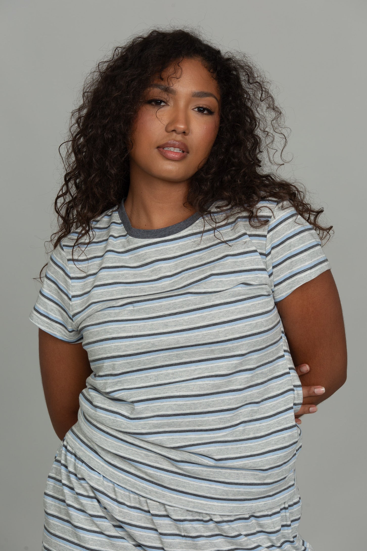 A person wearing a light gray and navy blue striped short-sleeve t-shirt and matching striped pants, posing against a solid gray studio background.