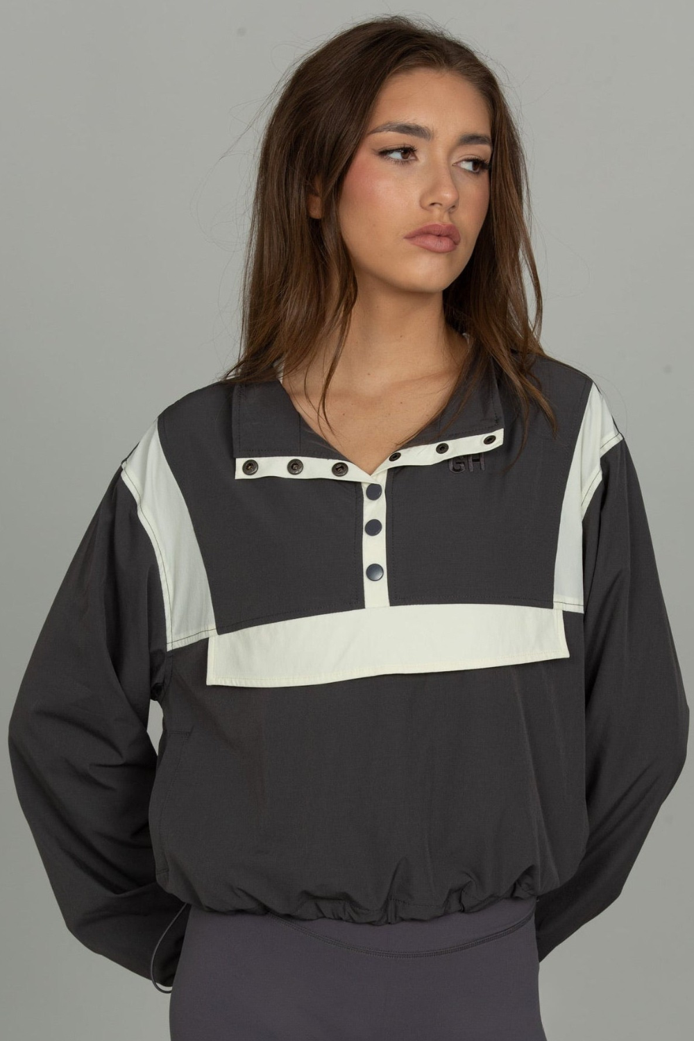 A woman wearing a dark gray and white color-blocked long-sleeve pullover top with a buttoned collar, shown against a plain gray studio background.